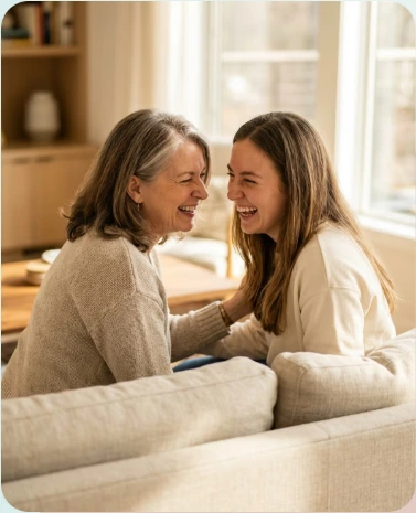 A mother and adult daughter smiling together at home
